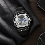 TIELBO T711 watch with black case, black bezel and black strap resting on charcoal fabric beside a dark wooden desktop; AI-assisted scene image