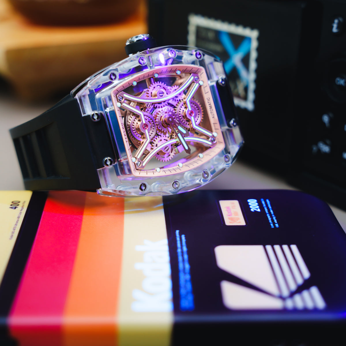 T832M Nightwalker with a rose-gold-tone openwork dial and black strap, displayed under violet lighting beside a camera and film packaging; original manufacturer photograph